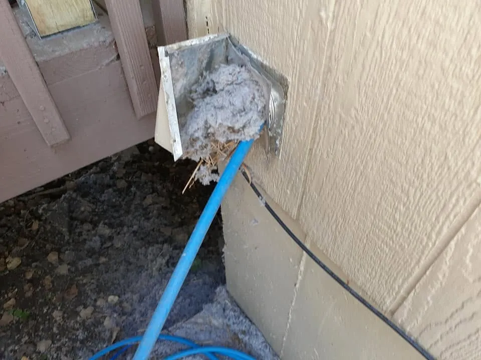 Dryer vent hood packed with lint, being cleared with a brush rod